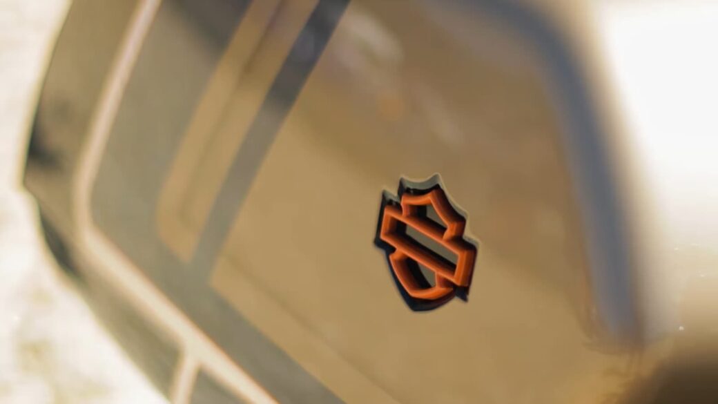 A close-up shot captures a distinctive orange and black shield-shaped emblem on a glossy surface